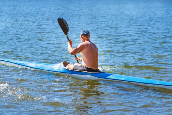 男は海岸近くの川に青と黄色のカヤックを漕いでいる。カヤックのコンセプト男が川のカヌーで泳ぐ。晴れた夏の日にボートに乗った男。青と黄色のボート. — ストック写真