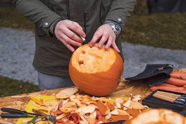 Cadılar Bayramı balkabaklarını kesme süreci. Erkeklerin eli bıçaklı, balkabağı kesikli. Erkeklerin elleri balkabağına desenler oyar. Cadılar Bayramı hazırlığı..