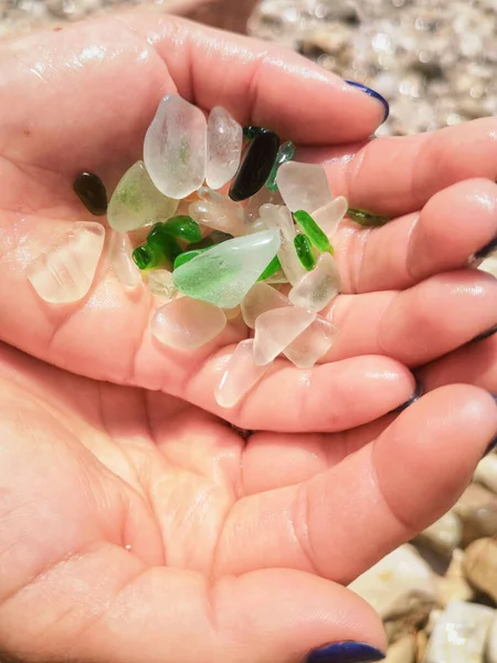 Кусочки морского стекла в руке. Зеленые куски стекла полированные на фоне моря крупным планом. Куча натурального пляжного стекла. Разноцветные куски полированного стекла . — стоковое фото