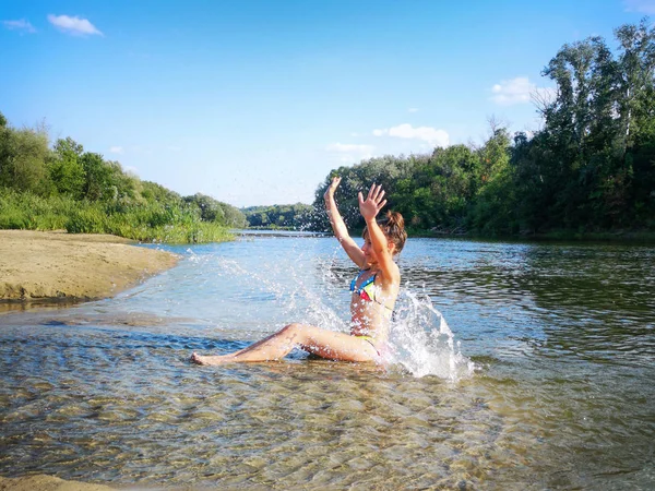 Nehir suyunda poz veren ıslak beyaz mayo giymiş seksi esmer kadın. Genç bir bayan suyla oynuyor. Yazın çekici bir kız. Nehirdeki kız su sıçratıyor.. — Stok fotoğraf