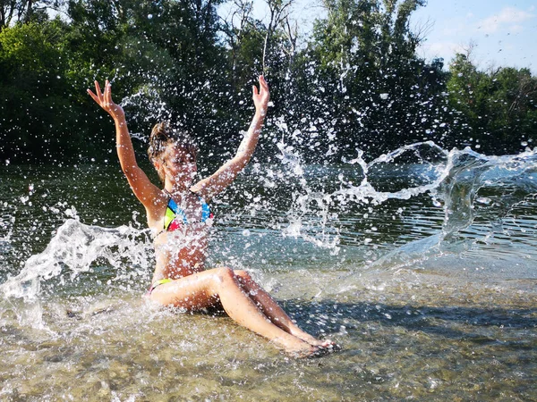 Сексуальна брюнетка у вологому білому купальнику позує у річковій воді. Молода жінка грає з водою. Приваблива дівчина влітку. Дівчина на річці бризкає воду . — стокове фото