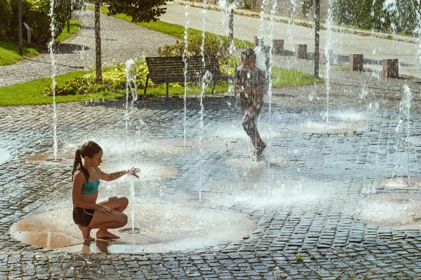 Kinderen op een zonnige warme dag buiten spelen in een waterfontein. Kinderen gelukkig in ondiep schoon water op de stad fontein op warme lichte zomerdag. — Stockfoto