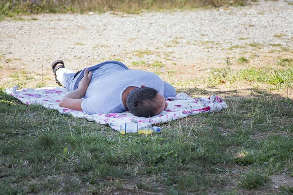 En mand hviler sig, sover på græsset på en sommersolskinsdag. Manden er træt. Hvil på det grønne græs . - Stock-foto