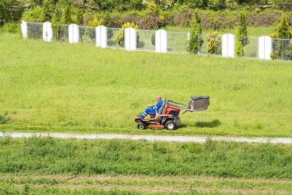 Un operaio che falcia erba nel parco cittadino. Sunny summer day.Mature uomo guida taglierina erba in un giardiniere soleggiato guida di un tosaerba equitazione in un giardinaggio . — Foto Stock