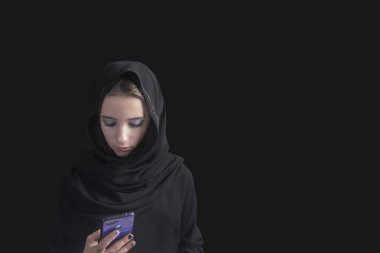 Siyah abaya giymiş Arap bir kız ve elinde telefon olan siyah bir geçmişi var. Müslüman Arap kız.