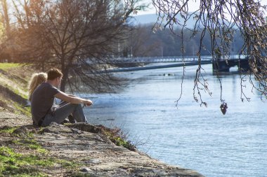 5.2019. Hangary. Genç bir çift nehir kenarında oturuyor. Nehir kenarında dinleniyor. Aşk ve insanlar kavramı