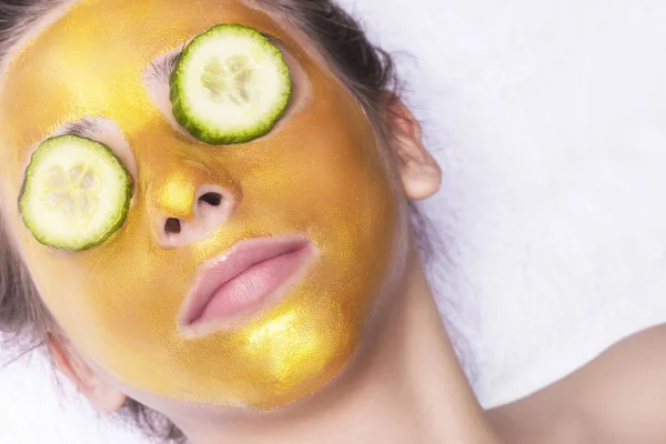 Mooi meisje met een cosmetische masker op het gezicht van gouden kleur. Close-up. Vrije ruimte. Vrouw gouden masker. Mooi model gouden gezichtshuid cosmetische verwijderen. Beauty huidverzorging . — Stockfoto