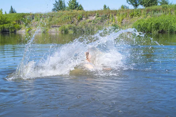 女性は湖の水に魚のようにジャンプし、泳ぎ、夏休みに時間を過ごすのを楽しんでいます。女性は川に飛び込む. — ストック写真