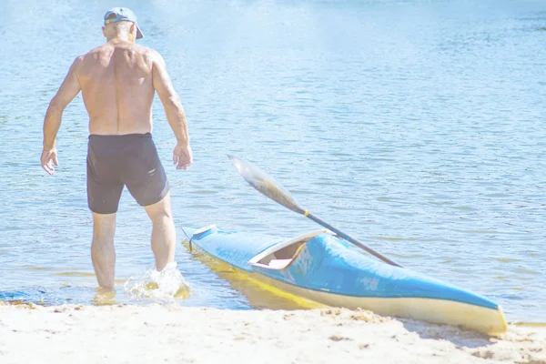 Muž pádluje na modrém a žlutém kajaku na řece u břehu. Koncept kajaku. Muž plave v kánoi na řece. Muž na lodi za slunečného letního dne. Modrá a žlutá loď. — Stock fotografie