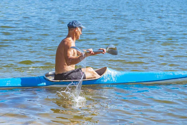 男子划着一艘蓝色和黄色的皮划艇在河岸附近的河里划着。 独木舟的概念。一个男人在河里的独木舟上游泳。 一个人在阳光灿烂的夏日坐船。 蓝色和黄色的船. — 图库照片