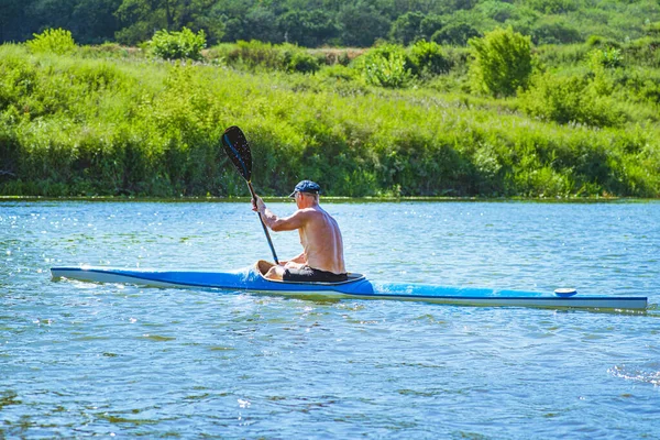 Muž pádluje na modrém a žlutém kajaku na řece u břehu. Koncept kajaku. Muž plave v kánoi na řece. Muž na lodi za slunečného letního dne. Modrá a žlutá loď. — Stock fotografie