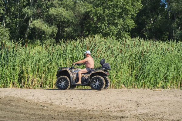 Un bărbat care merge cu bicicleta quad pe râu.Un bărbat pe o bicicletă Quad mergând pe plajă . — Fotografie, imagine de stoc