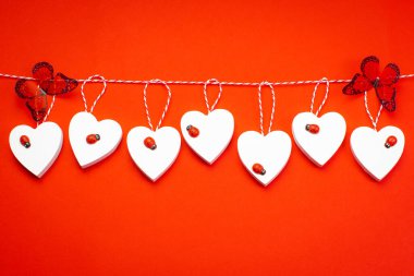 Valentine's Day. White wooden hearts on a red background and red butterflies. Blank for the designer. Valentines day concept. Greeting card. Copy space.