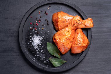Raw chicken legs in a marinade with spices on a black plate, marinated chicken legs for BBQ.Raw meat in the marinade.Top view.