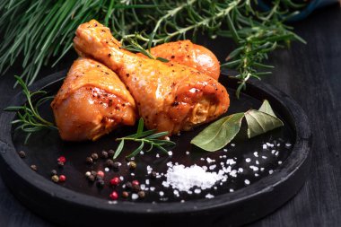 Raw chicken legs in a marinade with spices on a black plate, marinated chicken legs for BBQ.Top view.Raw meat in the marinade.