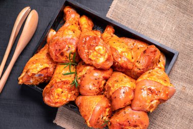 Raw chicken legs in a marinade with spices on a black plate. Top view.Chicken meat close-up.