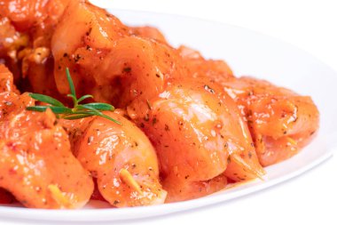 Raw chicken skewers in marinade with spices on a white plate. Top view. Chicken meat close-up.