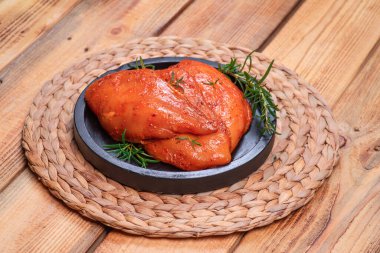 Marinated Chicken Breast with spices rosemary on a black plate. Raw meat in the marinade.