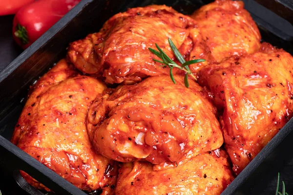 Chicken thighs. Spice.Raw chicken quilted in red, tomato marinade on a black plate and spices.Raw meat in the marinade.Dietary meat. Cooking.. Chili pepper .