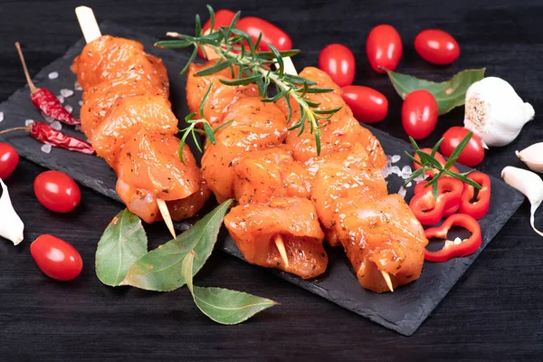 Raw marinated and spicy chicken skewers.Chicken meat close up. Raw chicken skewers in marinade with spices on a black plate and on a wooden table. Top view. Tasting diet meat.