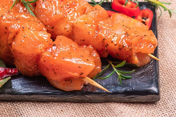 Raw marinated and spicy chicken skewers.Raw chicken skewers in marinade with spices on a black plate and on a wooden table. Top view. Chicken meat close up. Raw meat in marinade. Tasting diet meat.