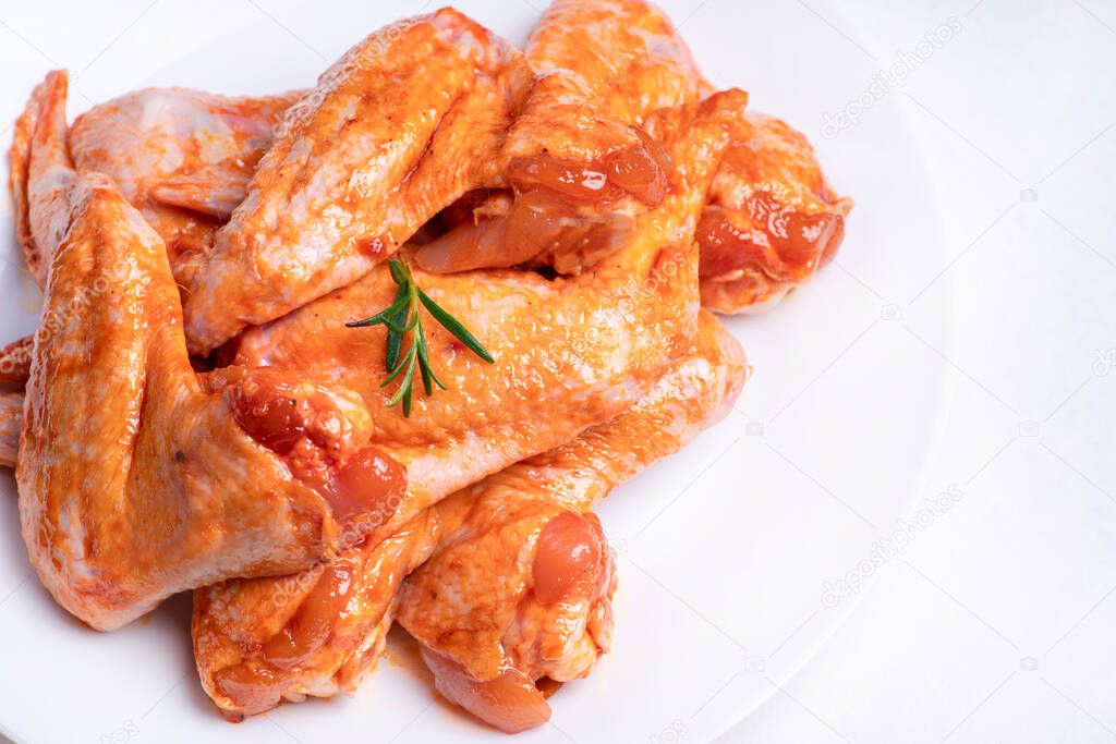 Raw chicken wings in a marinade with spices on a white plate.Top view. Chicken meat close-up.Raw marinated chicken wings for grill and bbq.Isolate.