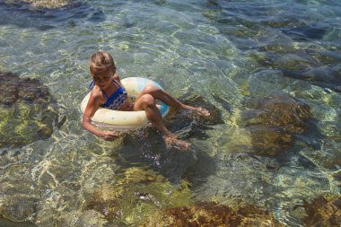 Denizdeki şişme lastik çemberde dinlenen güzel bir kız. Küçük kız yüzüyor ve deniz şişirilebilir bir daire içinde. Çemberdeki kız. Deniz Burnu. Sıcak yaz günü, tatil.
