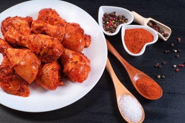 Beyaz bir tabakta çiğ tavuk salamura edilmiş bacaklar farklı baharatlar ve siyah arka planda biberler. Çiğ tavuk marine edilmiş et. Izgara bacak..