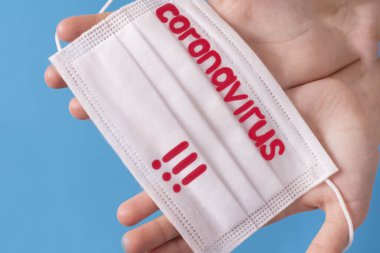 Coronavirus COVID karantinası kavramı. Eller mavi arkaplanda ve üzerinde Coronavirus yazısıyla koruyucu bir maske var..