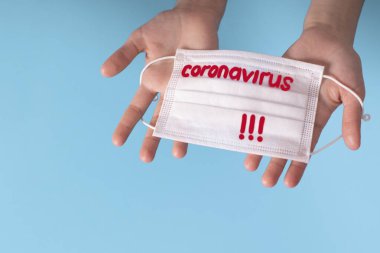 Coronavirus COVID karantinası kavramı. Eller mavi arkaplanda ve üzerinde Coronavirus yazısıyla koruyucu bir maske var..