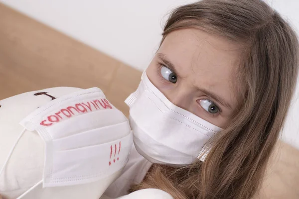 Little sad girl in a white T-shirt in a protective mask plays with a toy. . Wuhan epidemic outbreak. Dangerous Chinese Novel virus COVID-19.The girl is sad because of the virus.