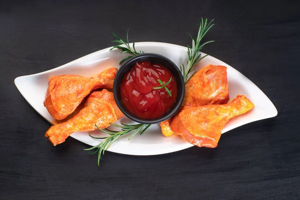 Raw chicken marinated meat. Grilled legs.Raw chicken marinated legs on a white plate with different spices and peppercorns on a black background.