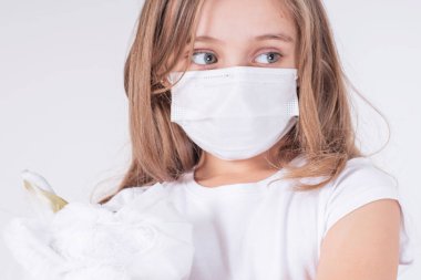 Dünya çapında koronavirüs salgını. Yüzündeki virüslerden koruyucu maske takan üzgün bir kız oyuncakla oynuyor. Coronavirus zatürree COVID-19.Koruyucu maskeli bir kız..