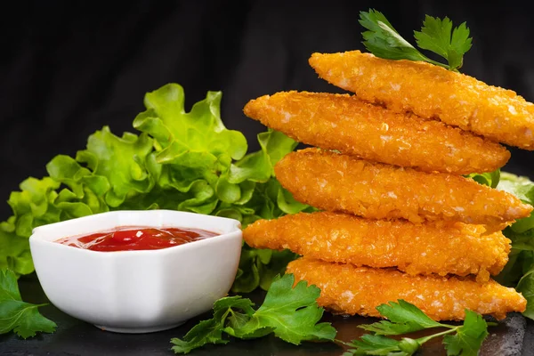 Tahta arka planda ketçaplı ekmek kırıntıları içinde leziz çıtır tavuk filetosu. Fast food. Lezzetli kızarmış tavuk göğsü şeritleri..