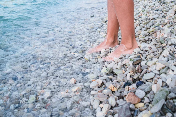 The bare feet of the girl go along the sea beach of sea stones. Sea rest.