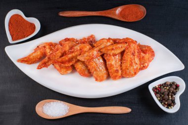 Baharatlı, beyaz bir yemek pişirme kabında marine edilmiş tavuk kanadı. Izgara tavuk kanadı tarifi..