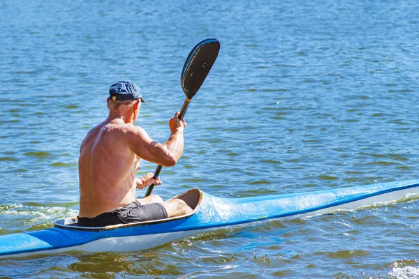 一个男人在河里的独木舟上游泳 蓝色和黄色的船 人在河岸附近的河里划着蓝色和黄色的皮划艇 皮划艇概念 — 图库照片