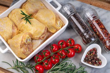 Pişirmeden önce çiğ tavuk budu. Sarı salamura içinde tavuk bacağı ve bir dal jilet, baharat, acı biber ve mermer mutfak tahtasının üzerinde bir dal domates..