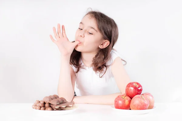 子供とチョコレート 明るい女の子はチョコレートとリンゴの間で選択します 健康的な食事 — ストック写真