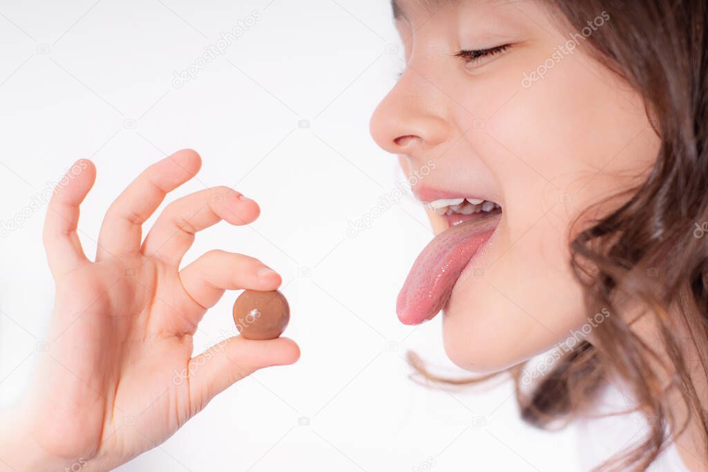 Cheerful girl plays and eats chocolate round sweets on a light background,world chocolate day.Children and chocolate.
