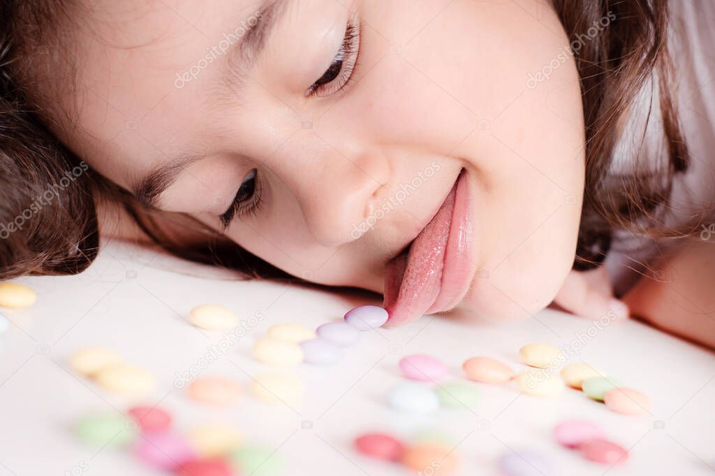 Children and chocolate. A cheerful girl plays and eats chocolate multi-colored round candies on a light background.Joyful girl with sweets.