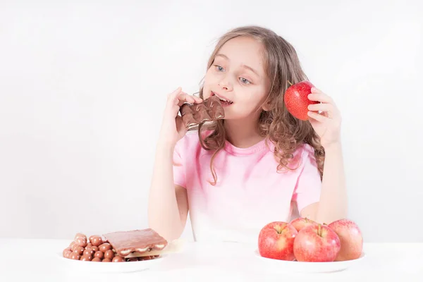 孩子和巧克力 一个快乐的女孩在巧克力和苹果之间做出选择 但选择是吃巧克力 健康的饮食 — 图库照片