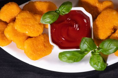 Ev yapımı fast food. Beyaz tabakta ketçap ve fesleğen yapraklı tavuk ekmeği..