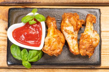 Seramik mutfak tahtasında kızarmış tavuk kanadı fesleğen yaprakları ve ahşap bir masada ketçap. Fast food.
