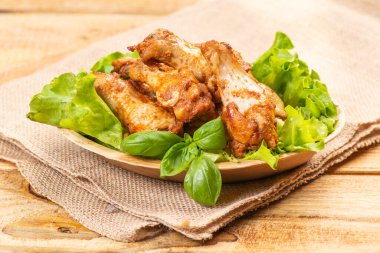 Fesleğen yapraklı ve marullu bir mutfak kasesinde kızarmış tavuk kanadı. Fast food.