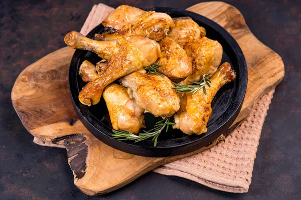 Grilled chicken legs on cutting board. Cooking chicken drumsticks.Chicken legs. Fried chicken legs on a wooden board on a black wooden background with a branch of razmarin.