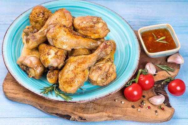 Grilled chicken legs on cutting board. Cooking chicken drumsticks.Chicken legs. Fried chicken legs on a wooden board on a black wooden background with a branch of razmarin ketchup and tomatoes.