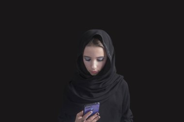 Siyah Arap elbiseli genç kız abaya 'nın elinde telefon var. Elinde telefon olan Müslüman bir kız. Müslüman kadın elinde tesettürlü akıllı telefon kullanıyor. .