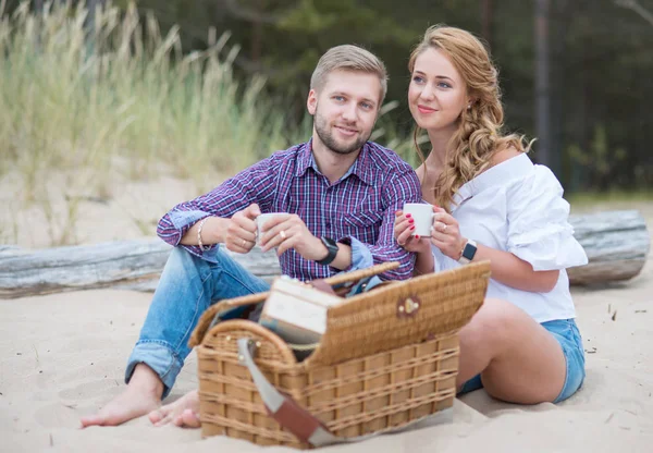 Jovem casal familiar na praia perto do mar fazendo um piquenique em — Fotografia de Stock