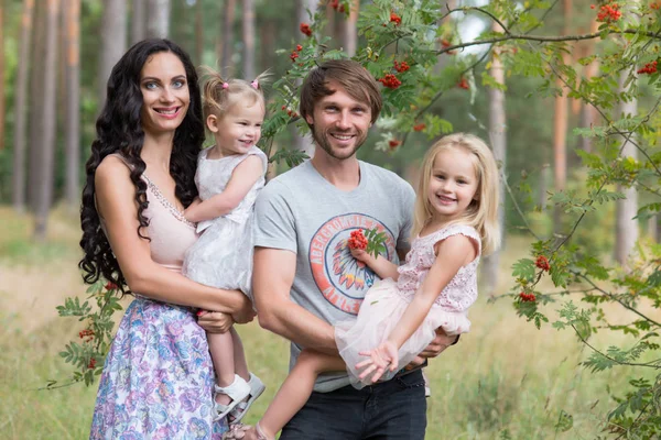 Hermosa familia joven con dos hijas caminando en el bosque — Foto de Stock